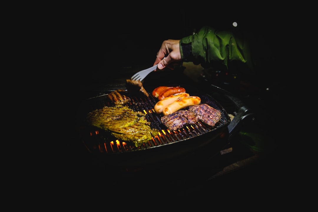 Person grilling various foods on a barbecue at night.